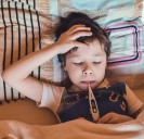 Foto: Kind mit Thermometer im Mund im Bett