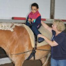 Das Foto zeigt eine Physiotherapeutin, die ein Pferd mit einem Schüler darauf am Langzügel führt.