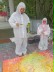 Das Foto zeigt zwei Mädchen in weißen Ganzkörper-Maler-Anzügen mit Pinseln und Farbtöpfen, die Farbe auf eine Leinwand a