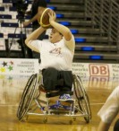 Das Foto zeigt einen Rollstuhlfahrer, der einen Basketball zum Wurf anhebt.