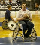 Das Foto zeigt einen Rollstuhlfahrer mit einem Basketball in den Händen, der zum Korbwurf ansetzt.