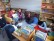 Das Foto zeigt eine Gruppe Schüler, die um eine vorlesende Lehrerin vor Bücherregalen sitzen, 